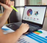 Person analyzing financial charts and graphs on a laptop with colorful documents, showcasing market analysis.